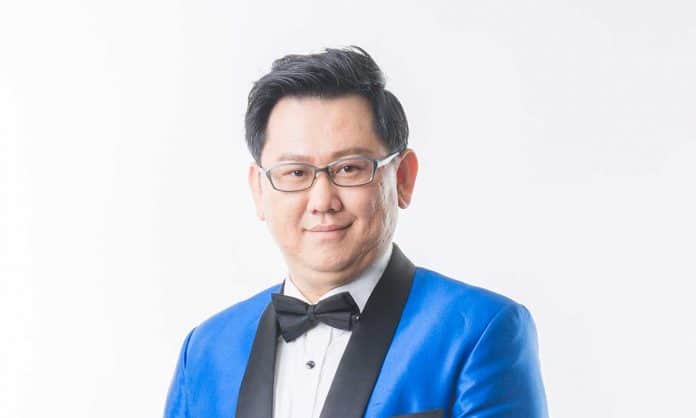 Bust portrait photo of Dato' Jacky Chee in a bright blue suit and black bow tie with a white background