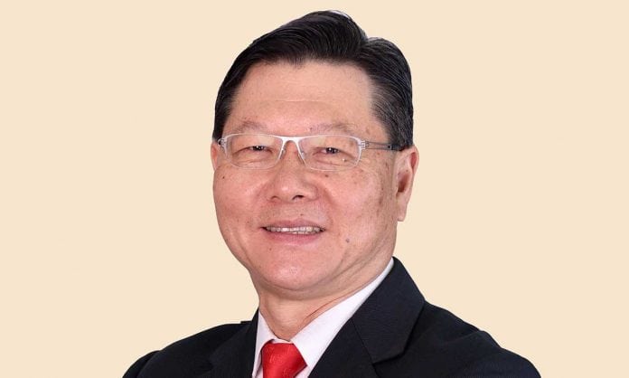 Closeup photo of Dato' Yeow Wah Chin in a black suit and red tie with a tan background