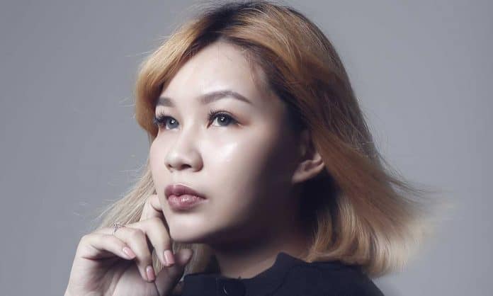 Closeup photo of Happy Kuah holding her right hand up her face in a 'thinking' pose while facing away from the camera with against a gray background