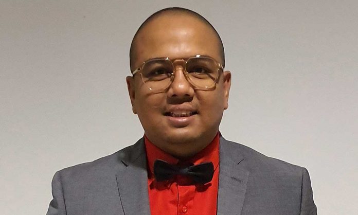 Bust portrait photo of Murtadza Zaim Mohd Zain in a red dress shirt, gray suit and black bow tie with a gray background
