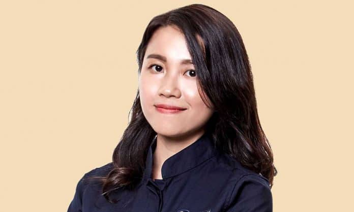 Bust portrait photo of Natalie Wong in a black top with a tan background