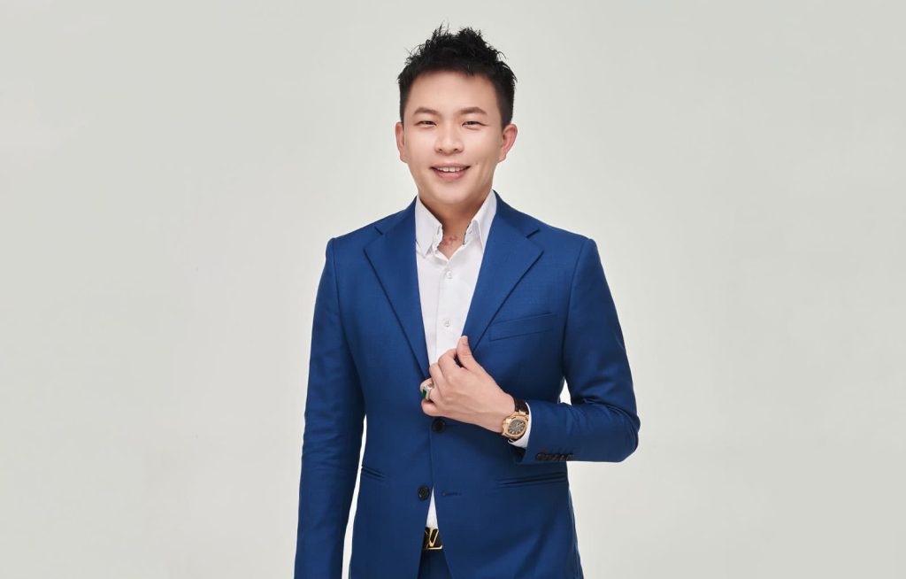 Half-body portrait of Cayson Goh with a white shirt and blue suit, one hand holding a lapel, with a white background