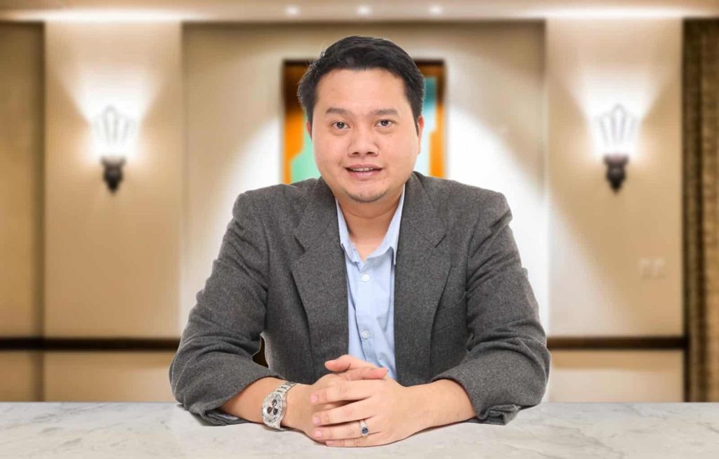 Portait photo of Dato' Captain Bakhtiar Aliff Bin Ibrahim in a light blue shirt and gray suit leaning forward on a table with hands clasped together atop