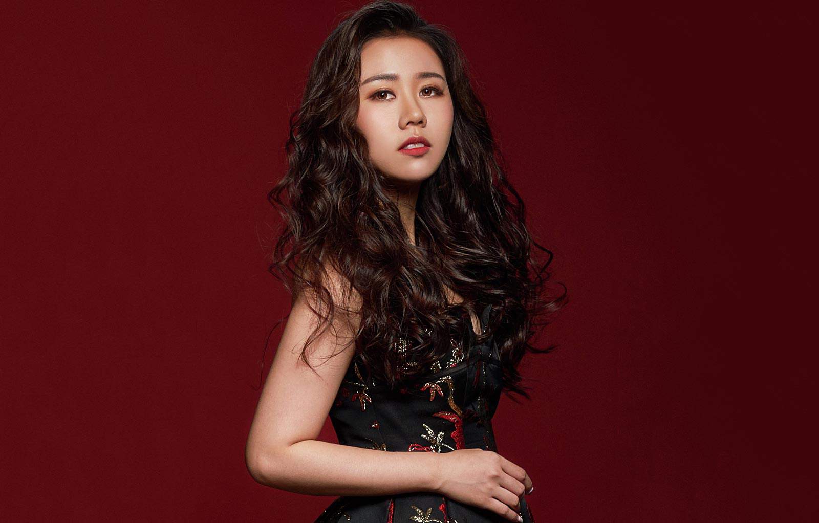 Medium closeup protrait photo of Evelyn Chan in a black dress with red and white accents, with a maroon background