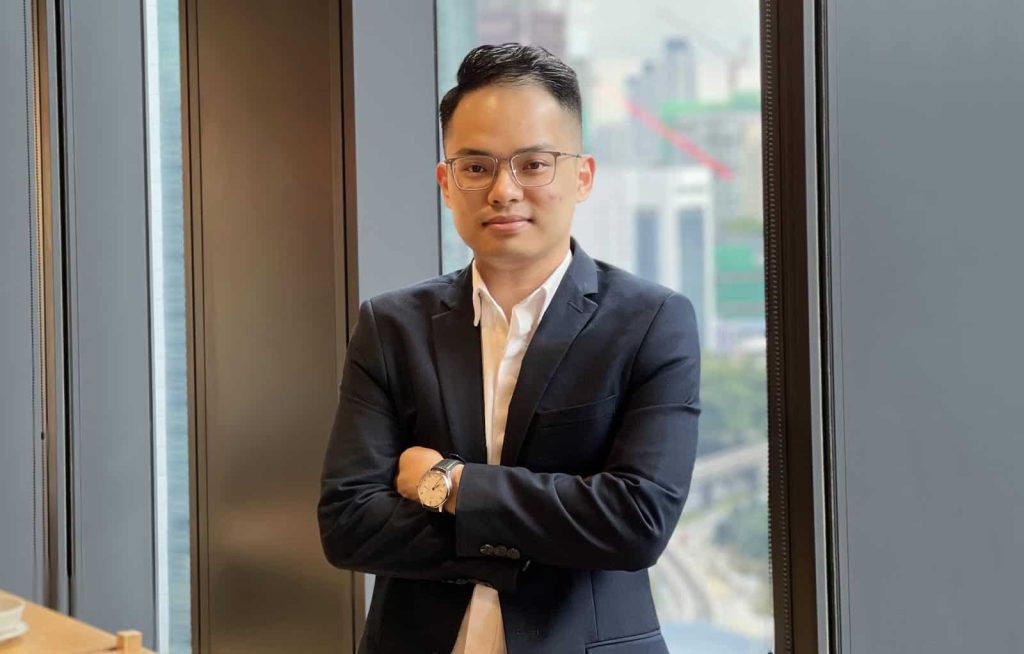 Half-body portrait photo of Gareth Yeoh in a black suit with arms folded with a window in the background
