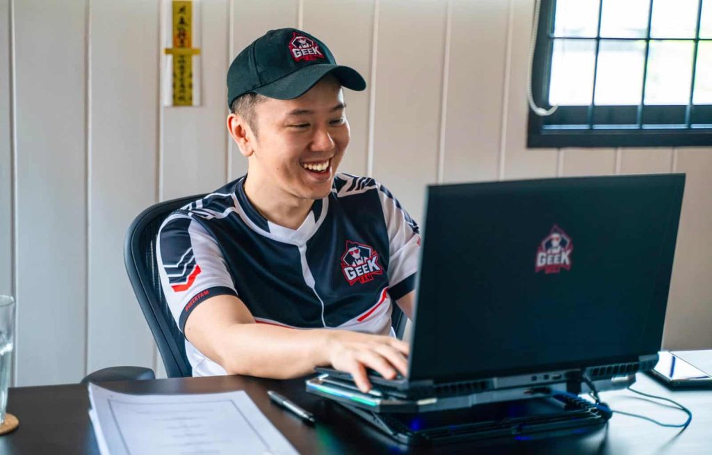 Photo of Lim Keat Kuang in a team uniform in, at an office desk, using his laptop