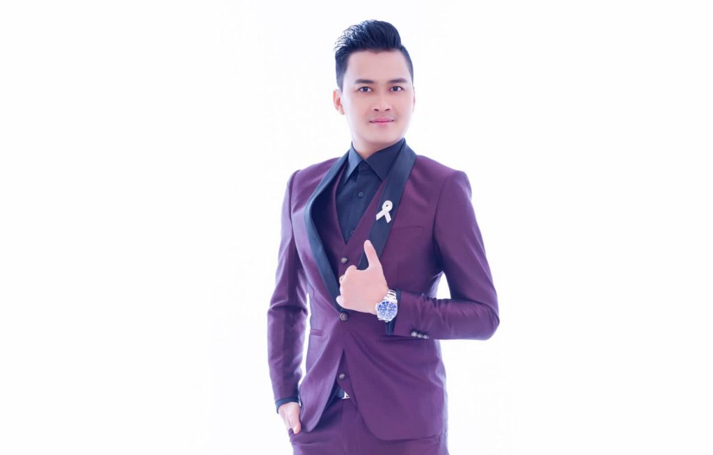 Half-body portrait photo of Lim Sen Tian in a black dress shirt and plum suit, posing in front of a white background with one hand over lapels