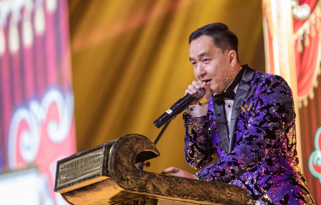 Photo of Paul Chen Joon in a purple suit giving a speech at a golden podium