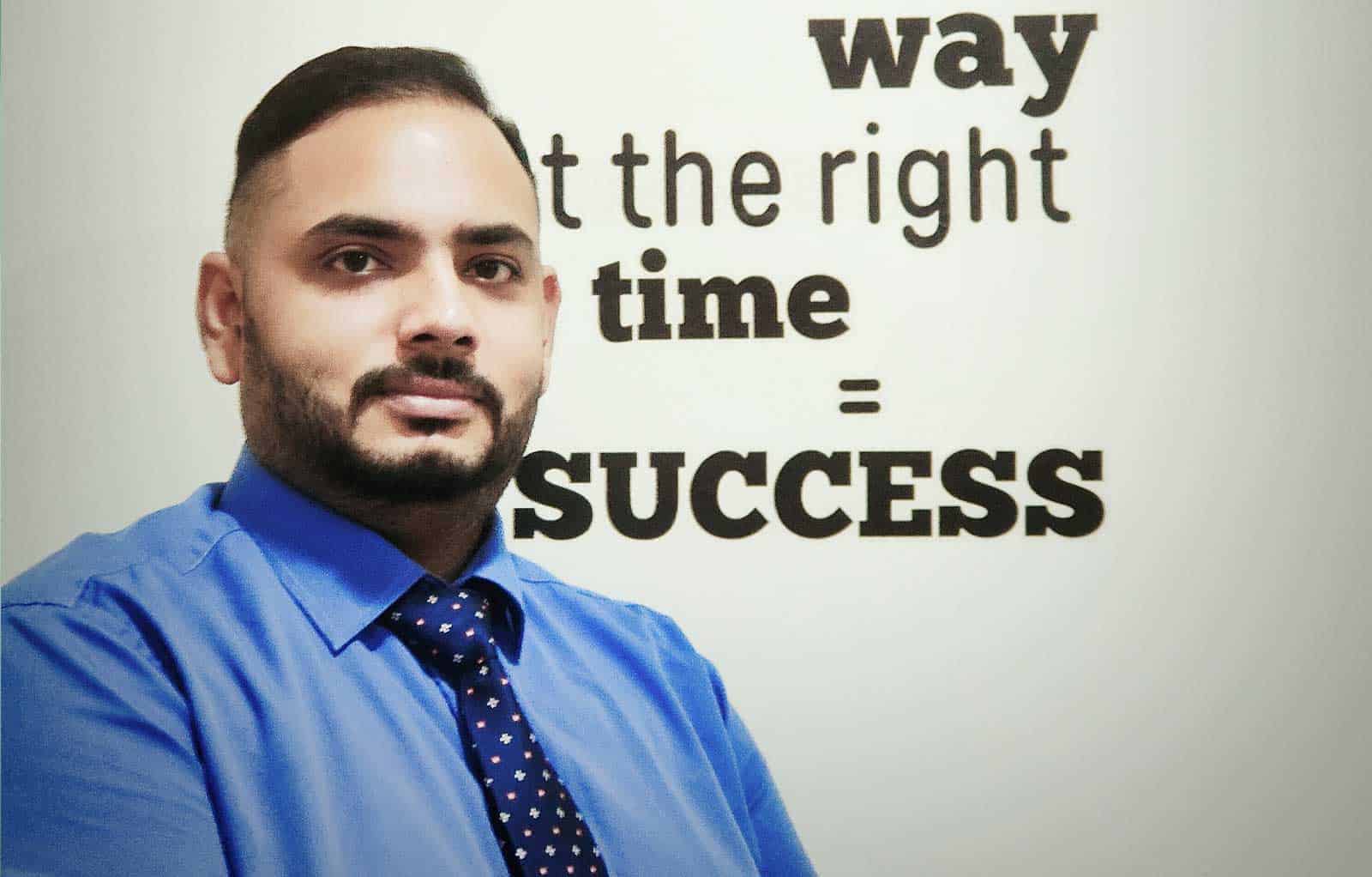 Bust portrait photo of Saswin Nair V Suresh in blue shirt and tie, with a cut off motivational quote in the background