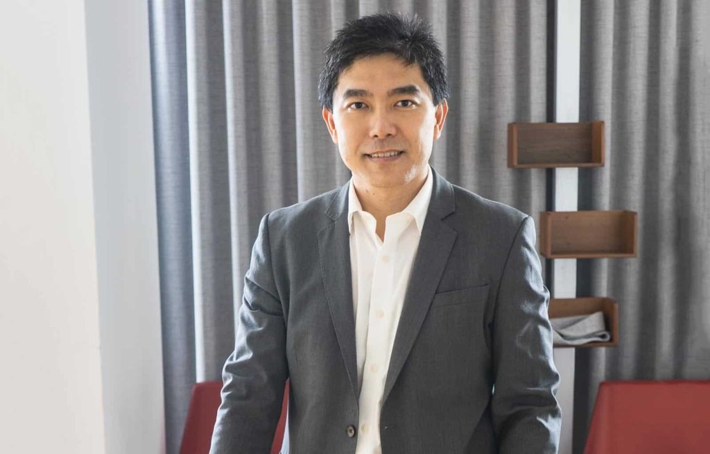 Portrait photo of Vincent Soh in a white dress shirt and gray suit, with gray vurtains in the background