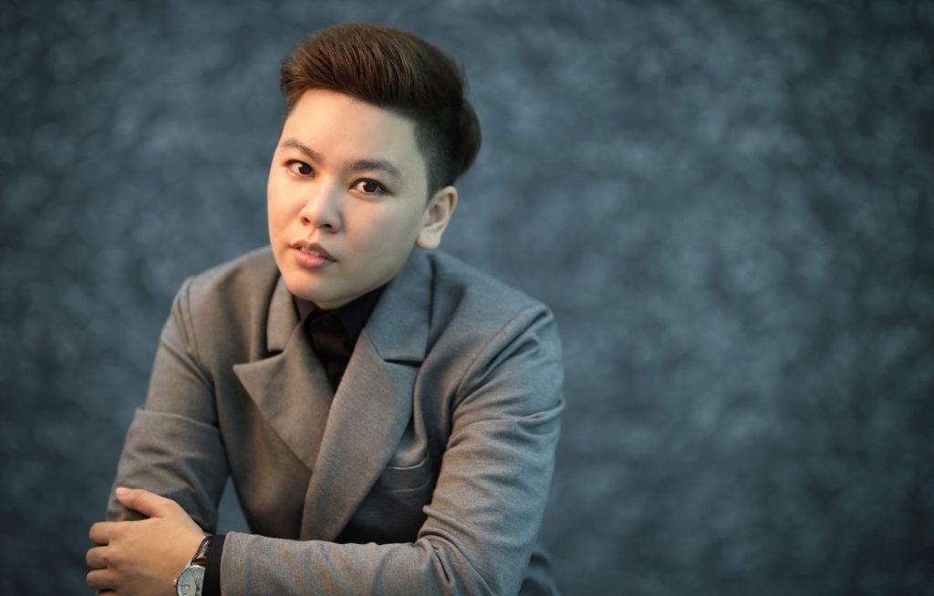 Portrait photo of YC Liang in a gray suit, leaning forward, arms folded, with a textured dark gray background