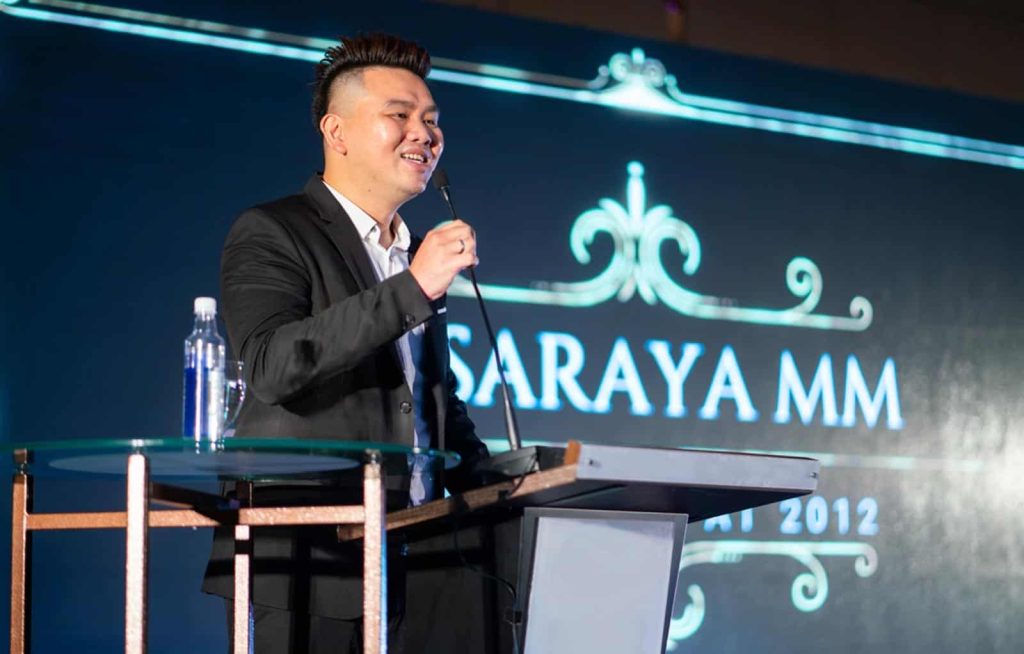 Wilson Cheng in a white dress shirt and black suit, speaking through a mic at a podium during a Pasaraya MM event